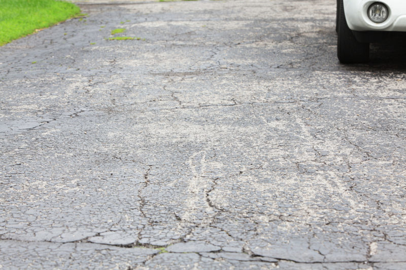 Cracked asphalt driveway with car parked