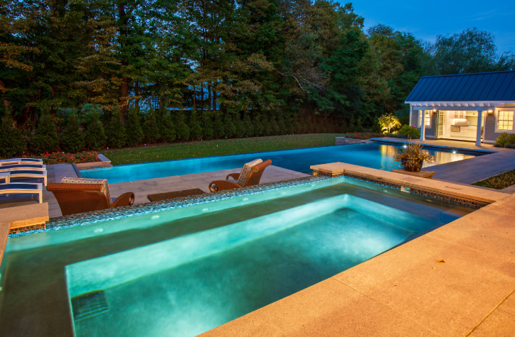 Outdoor pool with lights at night next to pool house