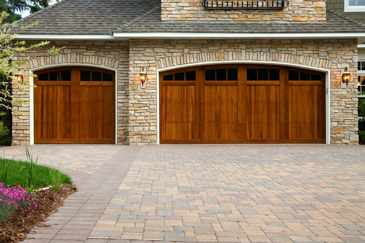 Pavers, wood custom garage doors, landscaping and beautiful stone exterior walls on a custom home.