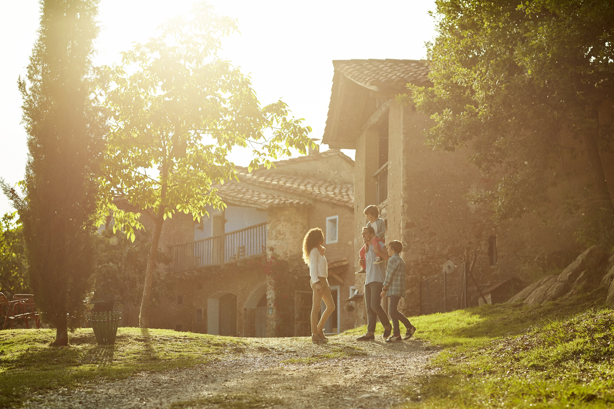 Full length of family standing on pathway against houses. Parents and children enjoying on sunny day. They are in casuals.