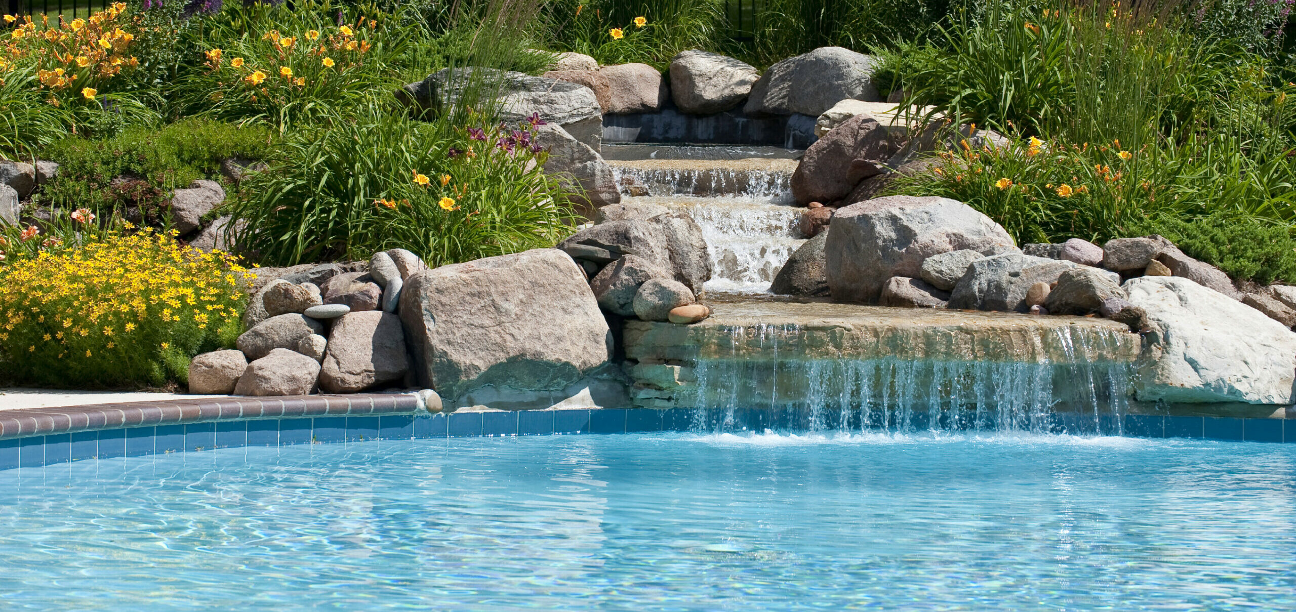 A swimming pool and waterfall by Ambrosio Landscape Solutions