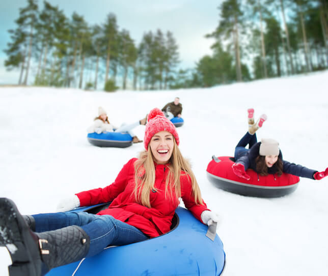 winter, leisure, sport, friendship and people concept - group of happy friends sliding down on snow tubes