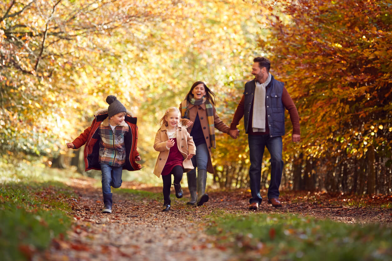 Family Walking Along Track In Autumn Countryside With Children Running Ahead