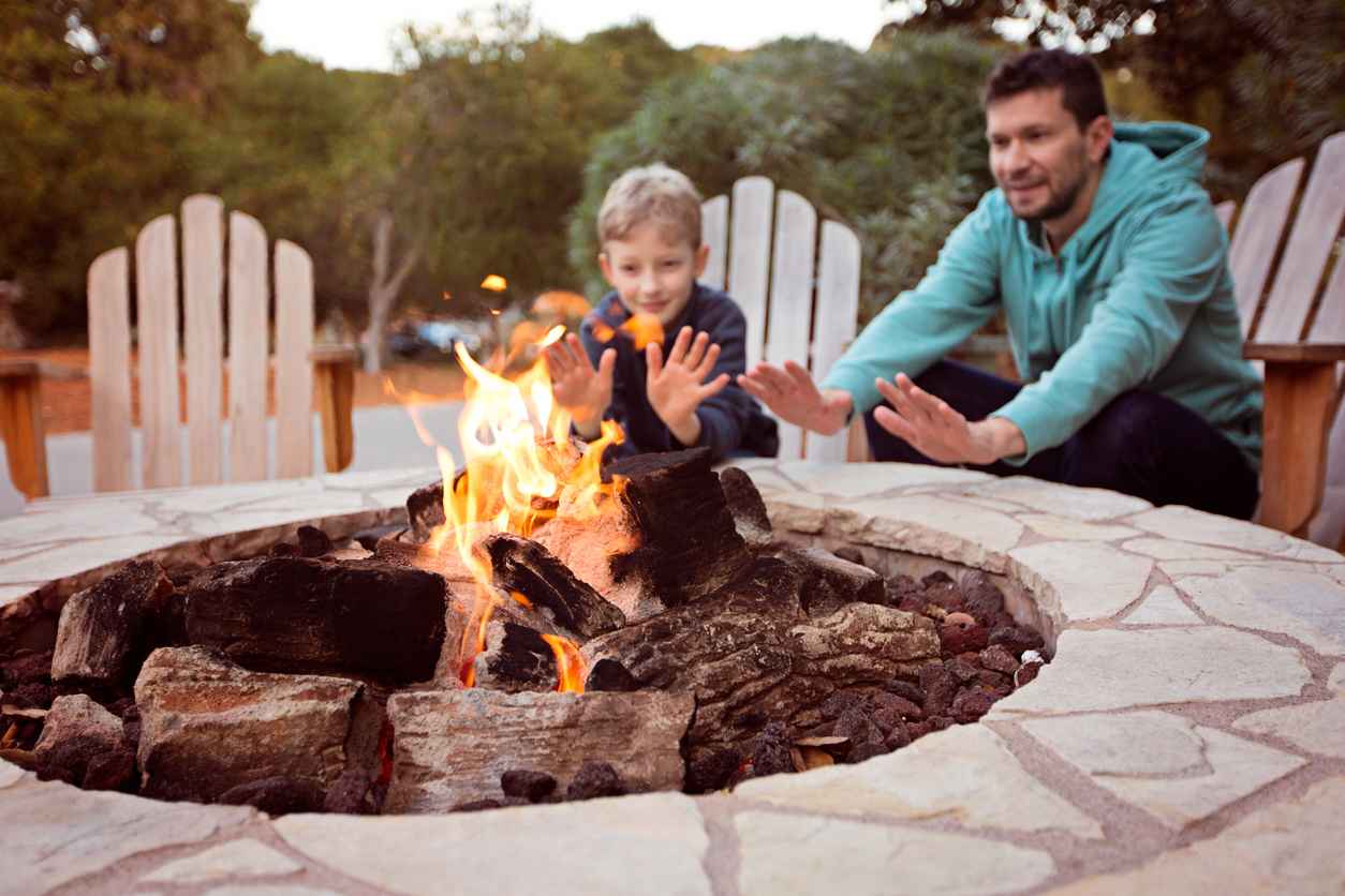 view of firepit and happy smiling family of two, father and son, warming their hands by the fire and enjoying time together in the background