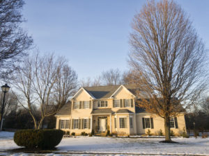 Colonial style two-story house with snow on ground and bare trees